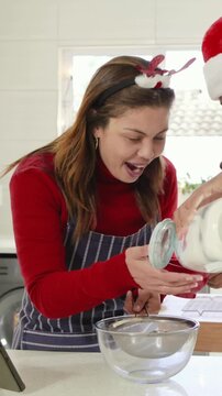 Vertical video: Pouring man tipping jar to sifter, woman apron using tablet, sifting holiday batter