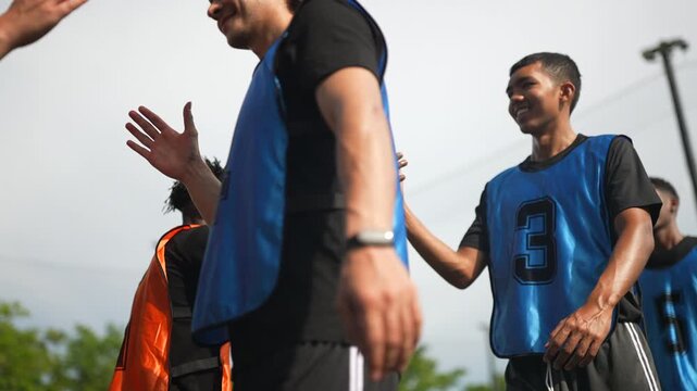 Football teams train and compete on outdoor fields under the supervision of dedicated coaches and referees. Two teams of footballers walk up and shake hands before practicing their football skill.