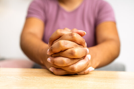 Woman's clasped hands praying on wooden table