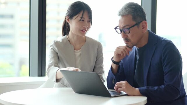 中高年のビジネスマンにパソコンを教えるビジネスウーマン