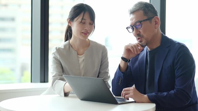 中高年のビジネスマンにパソコンを教えるビジネスウーマン