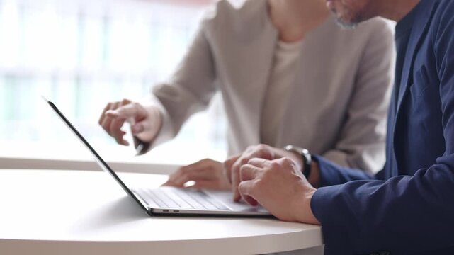中高年のビジネスマンにパソコンを教えるビジネスウーマン