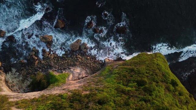 4K drone shot of Bali coastline with powerful sea surf washing over rocky formations at dusk. Premium tropical nature stock footage.