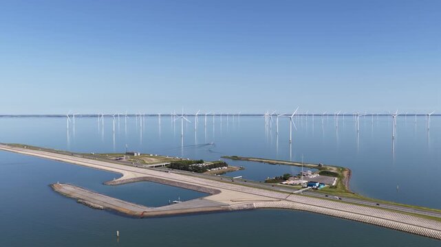 Aerial view of an offshore wind farm with turbines spinning in the calm sea, generating sustainable and clean electricity, while traffic crosses a long dyke under a clear blue sky