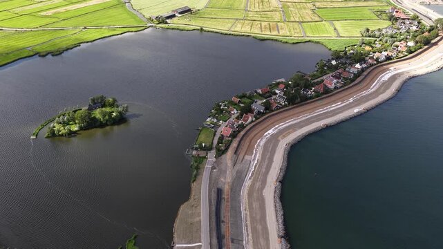 Aerial perspective showcasing extensive dike reinforcement and coastal protection work, with a strengthened levee protecting a waterfront village and surrounding dutch polder landscape from the sea