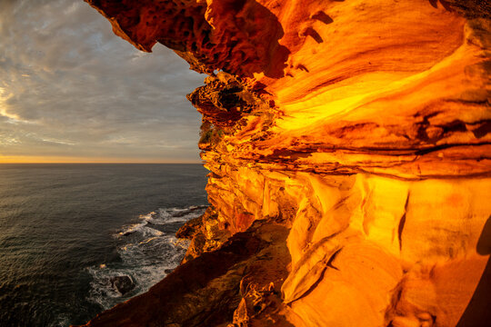 Sunrise illuminates sculpted sandstone cliffs and coastal rock formations overlooking the Pacific Ocean along the Sydney coastline, New South Wales, Australia.