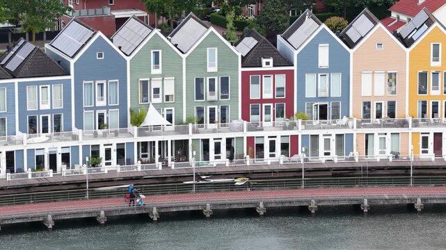 Aerial view of picturesque modern houses with solar panels along a canal in houten, netherlands, featuring vibrant architecture and people walking and cycling on a waterfront path
