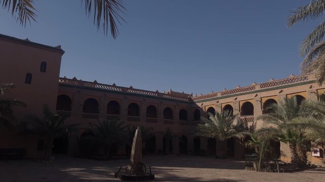 Large traditional Moroccan riad courtyard with arched colonnades palm trees and central fountain under blue sky