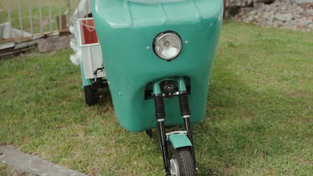 Restored vintage turquoise scooter with round headlight and sidecar parked on grass at wedding