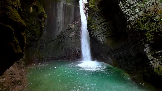 Cinematic shot of the hidden Kozjak waterfall flowing into a turquoise pool inside a dark karst cave. A serene example of ecofriendly nature travel and wellness.