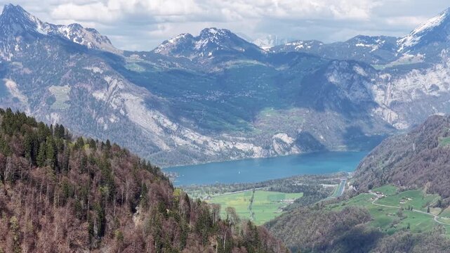 Walensee lake nestled in green valley below dramatic snowy Swiss Alps peaks with forested slopes