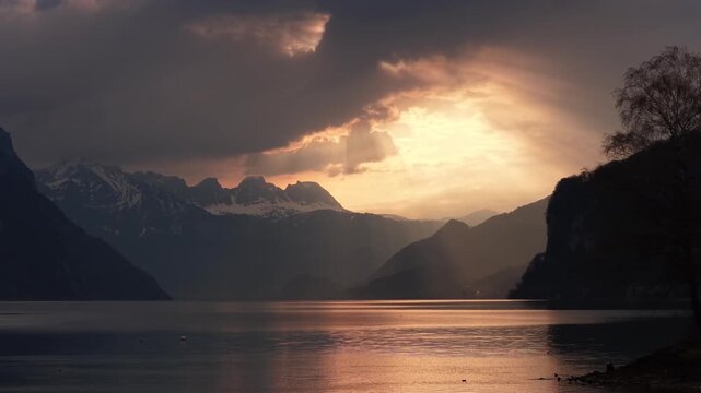 Golden dramatic sunset breaking through storm clouds over alpine lake and snowy mountain peaks Switzerland
