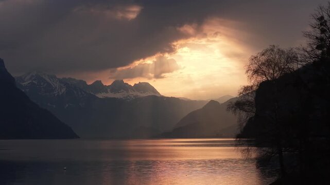 Golden sunset light breaks through dramatic clouds above Walensee in Switzerland. Sun rays illuminate the lake and surrounding alpine peaks, creating a breathtaking evening atmosphere.