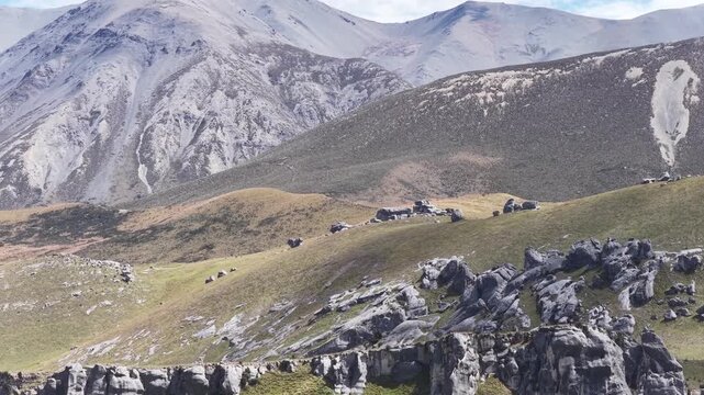 Scattered limestone boulders on green hills below snow capped mountains at Castle Hill New Zealand