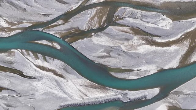 Drone top-down view of turquoise braided river channels winding through glacial sediment plains in New Zealand's South Island.