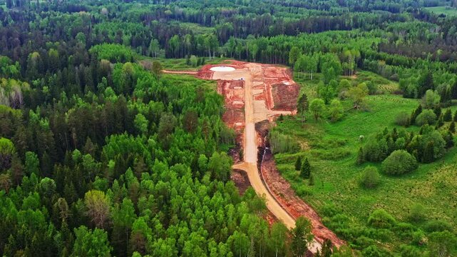 Aerial view of a wind turbine construction site with a new access road in a large green forest
