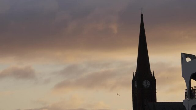 Moody sunrise over the west coast of Scotland, features a dramatic gothic church tower silhouette with a slow-motion bird flying through eerie, overcast morning clouds