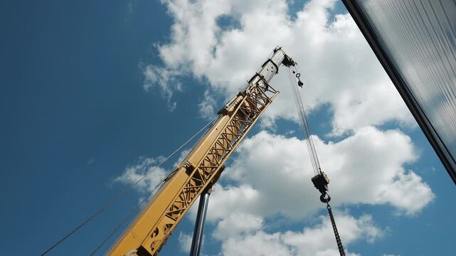 Mobile crane rotating its boom with lifting hook during heavy industrial cargo handling. Construction equipment, rigging operation and industrial logistics at a worksite.