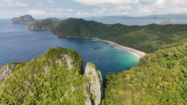 Stunning high-angle aerial drone shot of a secluded sandy crescent beach hemmed in by lush jungle-covered mountains and steep karst limestone cliffs along the scenic coast of Palawan, Philippines.