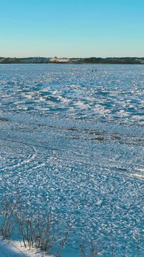 Vertical view of a frozen coastline during winter in Rewa, featuring jagged ice floes, snowcovered ground, and a clear blue sky. Cinematic winter landscape for travel and climate content.