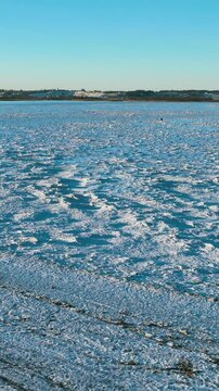 Cinematic vertical drone shot of a frozen sea surface covered in white ice floes and snow during a clear winter day in Rewa.