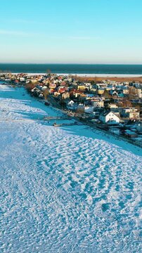 A stunning cinematic vertical drone shot showing the frozen Puck Bay and snowcovered houses in Rewa, Poland. Perfect for winter travel and climate change storytelling.
