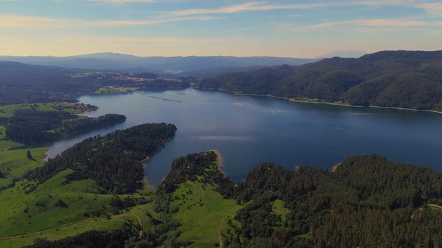 drone flight following the curved shoreline and dense pine forests enclosing Dospat Reservoir in the Rhodope region at sunset