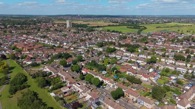 Chadwell Heath rooftops orbit beside Chad Park as drone pans toward the A12 corridor and Ferrier Point tower block on the Romford skyline, showing suburban streets and estate housing.