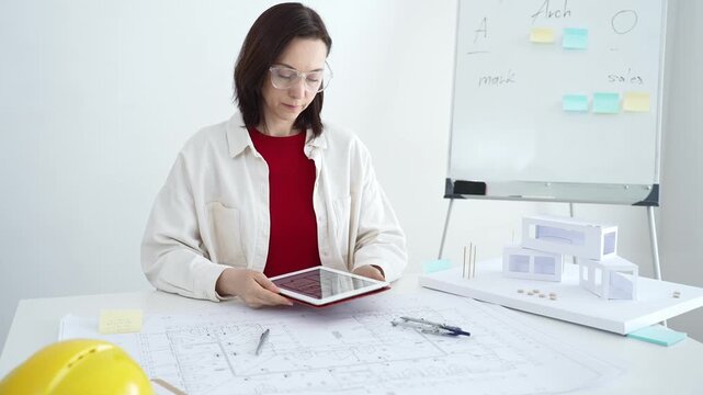 Architect working on new residential project using laptop, reviewing blueprints and drafting floor plans for modern building design with a 3d model on office desk