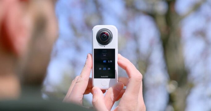 Person's hands operating an Insta360 X4 360 degree camera with a touchscreen interface outdoors