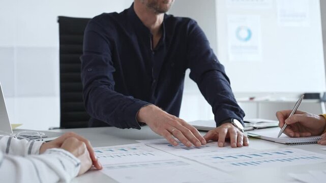 Professional colleagues reviewing financial charts, collaborating on strategic planning, gesturing toward data visualizations during corporate meeting in office. Business people concept
