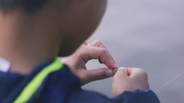 Close-up of hands baiting a fishing hook, outdoor fishing preparation
