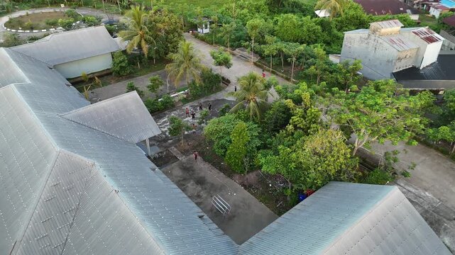 An aerial photo taken by a drone shows poor, undereducated children playing in a courtyard between tin-roofed village houses surrounded by lush tropical trees in a slum in Indonesia.