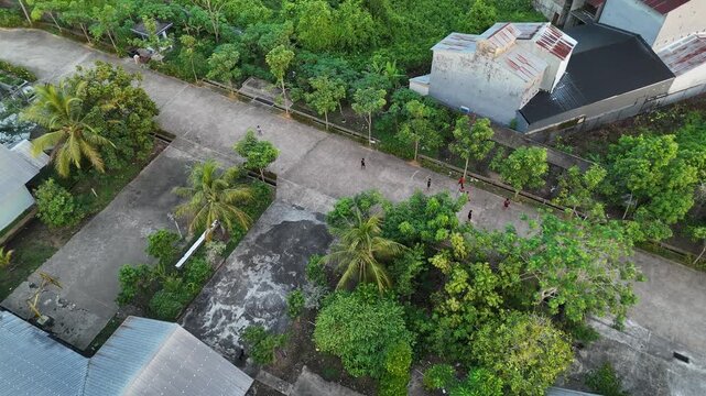 An aerial view showing poor village children playing on a village road lined with lush tropical trees and coconut palms in Indonesia.