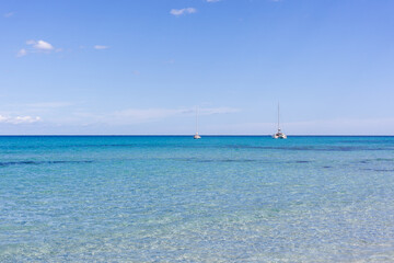 Obraz premium Calm turquoise sea in Sardinia, Italy. Shallow waters near the coastline. Sailboats floating on the serene Mediterranean Sea.