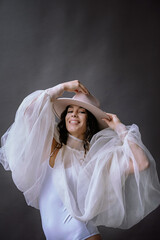 Fototapeta premium Elegant woman in white outfit, posing with hat, dark backdrop