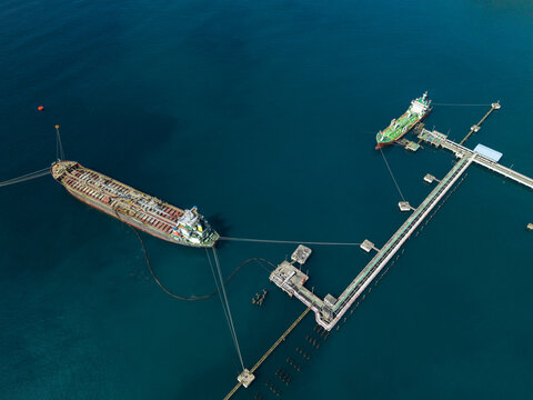 Aerial view of the Oil Fuel Terminal Port with large oil tankers moored at the industrial jetty in the deep blue sea in Manggis, Bali, Indonesia.
