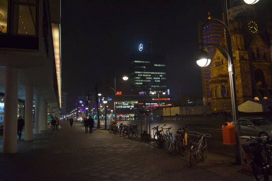 Berlin, Germany - January 25, 2016: Night view of Budapester strasse next to Breitscheidplatz with the illuminated Kaiser Wilhelm Memorial Church, Europa-Center tower, parked bicycles and pedestrians.