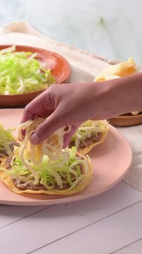 Woman's hand adding Oaxacan string cheese to a tostada. Mexican food. Slow motion