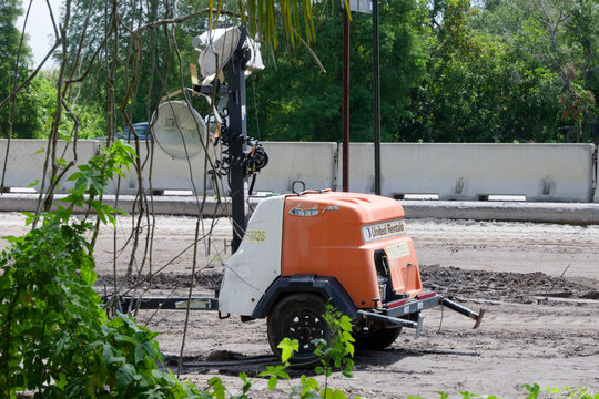 Orange portable light tower and rental generator parked on a muddy construction site. Editorial Use Only June 24, 2026 St. Petersburg, FL USA near highway concrete barriers, surrounded by greenery and