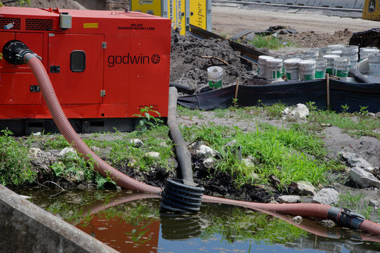 Red dewatering pump with large corrugated hoses discharging into a muddy retention pond. Editorial Use Only June 24, 2026 St. Petersburg, FL USA at an active construction site, showing drainage, erosi