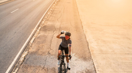 Obraz premium A cyclist battles a heat wave on a hot road, pouring water. Overhead view with clear copy space in the background, perfect for news and advertising.