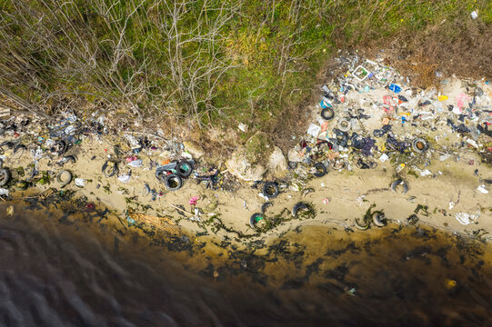 Aerial view of Lake Varna shoreline polluted with discarded tires, plastic waste, and debris scattered along the sandy beach in Varna, Bulgaria.