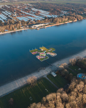 Aerial view of the puzzle-shaped floating island in Maarsseveense Plassen, with colorful pathways and green spaces, surrounded by calm water and parkland in Maarssen, Utrecht, Netherlands.