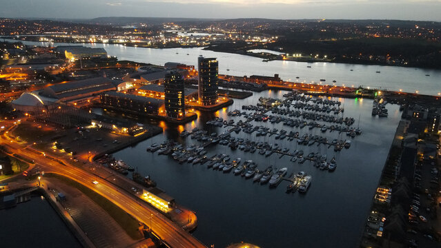 Aerial view of the marina at dusk with modern apartment buildings, rows of moored boats, and illuminated waterfront streets in Chatham, England, United Kingdom.
