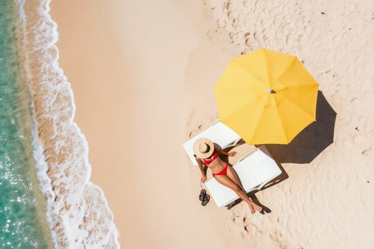 Woman in red bikini and straw hat relaxes on beach chair. Yellow umbrella shades her. Gentle waves lap sandy shore. Turquoise ocean water gleams brightly. Enjoying tropical paradise.