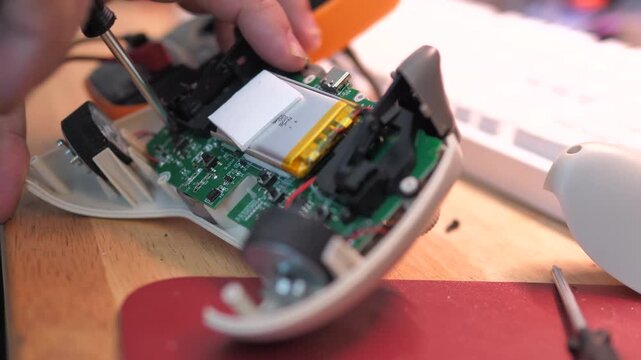 Close-up of a person repairing a game controller, using a screwdriver to work on the internal circuit board during DIY electronics maintenance