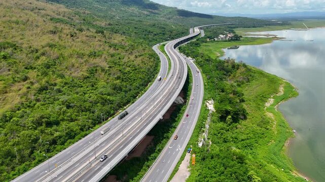 Aerial view of highway running along river and green hills. Transportation, infrastructure, travel and logistics concept