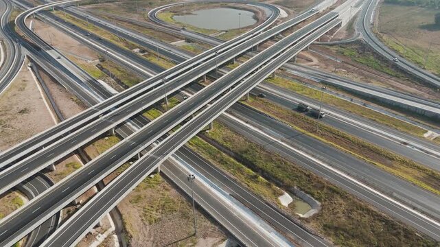 Aerial footage of a modern highway interchange stretching through a green rural landscape, The scale structure and flow of a major transportation infrastructure
