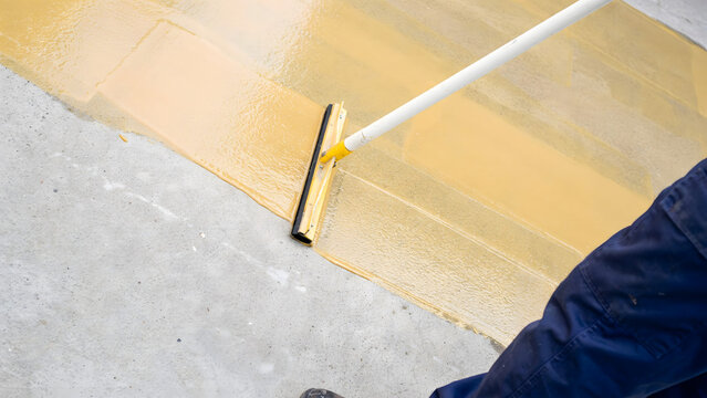 Worker using a squeegee to spread resin coating on a concrete floor